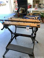 Full view of Black & Decker Workmate workbench and vise with wooden plank top, multiple holes, and a vise mechanism, along with assorted tools on table.
