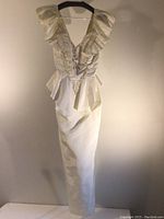 Full view of the satin floor-length dress hanging, showing the off-white color, peplum waist, and gather details on the skirt.