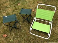 Photo of two green carrying camping stools and one folding beach chair on grass from front angle.