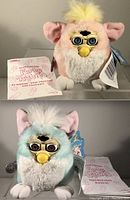 Two Furby Babies shown with original instruction and English dictionary manuals, tags attached, pale pink/yellow and mint green/white with large ears, soft fur, yellow beaks, and large eyes.