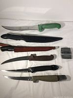 Full set of six fishing cutting utensils displayed on a white surface including sheaths and small sharpener.