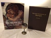 Three items displayed: Michelangelo art book, Art Treasures of Europe book, silver cup.