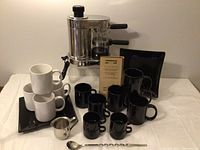 Full set showing cappuccino maker, mugs in black and white, espresso cups, black square plates, stainless creamer, spoon, and original instruction manual