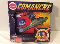Front view of Cox Comanche helicopter in original box showing model inside along with box graphics, including brand and model designation.