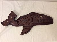 Full view of the wooden grey whale sculpture showing carved body and inlaid tail fins.