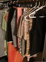 Clothes hanging in a closet showing some tops, skirts and dresses in various colors and patterns including black, white, peach, green, and patterned fabrics