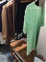Photo showing several hanging garments including the mint green crocheted top and skirts/jackets behind it.