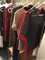 Photo showing multiple tops and dresses on hangers, including sequined and patterned tops and dresses in black, gold, red, and blue.