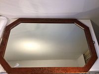 Full view of rectangular wood framed mirror with bevelled glass, wood frame medium brown with brass Greek key pattern.