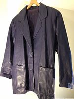 Front view of purplish blue leather jacket showing lapels, button closure, two front pockets, and long sleeves.