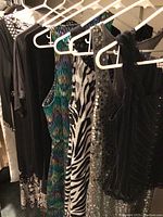 Group of dresses and tops on hangers showing various colors, patterns, and textures including black, sequin, and printed fabrics.