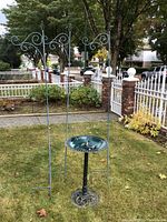 Full view of two shepherd hooks standing in the grass alongside the metal bird bath showing scale and condition.