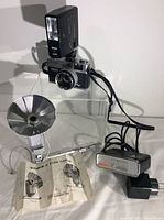 Photo showing Canon GIII QL17 camera with an attached flash, the Soligor BL Deluxe Flash with its metal clip mount, and instruction manual for the Soligor flash.