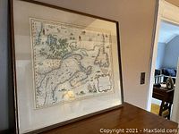 Framed reproduction map of early Canada displayed on a sideboard with visible frame and glass reflection.