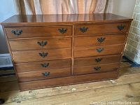 Front view of rectangular wooden dresser with 6 drawers and metal handles on wooden floor.
