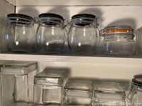 Four round glass jars with metal clamp lids and black rubber seals on a shelf, along with four rectangular glass jars with glass lids below