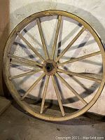 Full wheel showing 12 wooden spokes, wooden rim painted faint yellow, iron rim outer edge and overall shape.