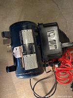 Side view of blue horizontal air tank with black motor housing and orange coiled air hose. Various instructional and safety labels affixed to tank and motor housing.