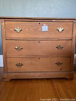 Front view of the chest showing three drawers with brass decorative pulls and keyholes, wood grain visible, slight wear marks at bottom edge.