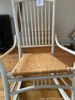 Front view of the small white painted wooden rocking chair showing the woven wicker style seat and spindle backrest.