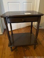 Front view of small dark brown painted wood table showing the drawer and bottom shelf