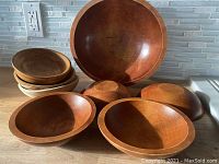 The set of eight wooden bowls arranged on a surface showing the large and smaller salad bowls along with three assorted smaller bowls.