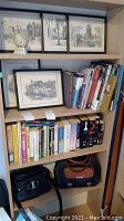 Overview of a wooden shelf unit with four framed 9x11 black and white prints on top shelf, books arranged on middle shelves, and two purses on bottom shelf.