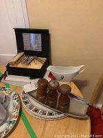 Wide view of boxed cheese board and tools alongside salt and pepper grinders on platter and white gravy boat on table