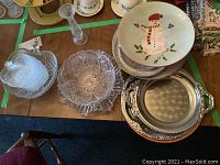 Overview photo of two clear crystal/glass serving pieces, artisan glass plate, stack of snowman decorated bowls, and silver serving tray.