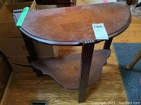 Front view of the wooden demi lune table showing the top, legs, and lower shelf with visible wear and scratches.
