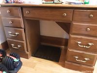 Photo showing a wooden desk with six drawers and brass handles, moderate scratches visible