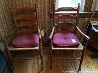 Five wooden dining chairs, including two with arms and three without, all with rush woven seats and red cushions, arranged in a room by a window.