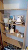 Shelf with white ceramic pitcher and basin, Disney snow globe, Disney princess figurine, tin container, framed item, and small ceramic dish.