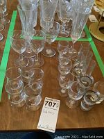 Top-down view of assorted clear drinking glasses arranged on a wooden surface showing groups of wine glasses, champagne flutes, and shot glasses with a tagging label numbered 707.