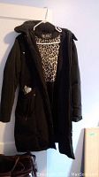 Front view of black Nuage jacket hanging on white hanger showing leopard print lining inside, two front zippered pockets, and hood.