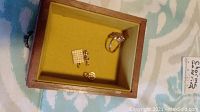 Wooden box with yellow interior showing ring at top right and two charms at bottom left