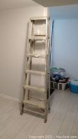 Full view of 6ft aluminum step ladder upright in a room corner, showing paint marks and wear on the rungs and rails