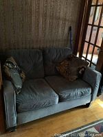 Front view of gray velour love seat with two decorative cushions.