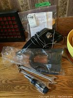 Photo showing MVP car vacuum, coiled cord, detachable nozzle in plastic bag, two metal open-end wrenches, and flat-head screwdriver.