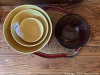 Three nested yellow ceramic mixing bowls beside two dark amber glass bowls on a decorative Florentine style rug and tray.