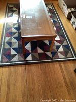 Photo of the acrylic area rug under a wooden table on hardwood floor showing pattern and condition.