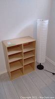 Shelving unit with lamintate over MDF next to tall white floor lamp against white wall.