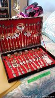 Case open showing two layers of silver plate flatware with ornate patterned handles, including forks, knives, spoons, and serving utensils on red fabric lining.