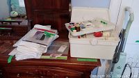 View of plastic sewing box on wooden dresser beside folded clear plastic suit bags and papers