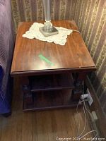 Photo of a wooden side table showing the top surface, bottom shelf, and turned legs with a lamp placed on top, to demonstrate the condition and style.