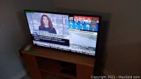 RCA 32 inch TV displaying news channel, placed on light wood TV stand.