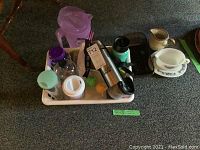 Photo of various bottles, pitcher, thermos, gravy boat, and other kitchen items on white tray and gray floor
