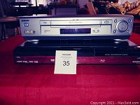 Photo showing Sharp Aquos Blu-ray DVD player in black and Sony Hi-Fi stereo VCR stacked on top, both presented on red surface with a MaxSold label.
