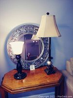 Photo showing both lamps and the ornate round mirror on a wooden octagonal table in a living room corner.