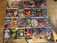 Top view photo of 28 Walt Disney VHS movie tapes arranged in rows on the floor, showing cover art clearly for identification.